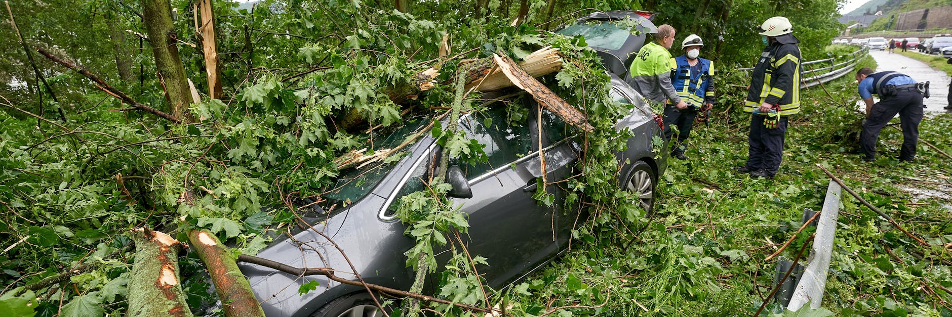 Feuerwehrleute stehen hinter einem Fahrzeug an der Bundesstraße 42, das während eines Gewitters von umstürzenden Bäumen begraben wurde. Der Wagen war geparkt, Menschen kamen nicht zu Schaden. 