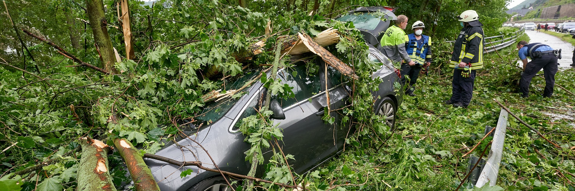 Feuerwehrleute stehen hinter einem Fahrzeug an der Bundesstraße 42, das während eines Gewitters von umstürzenden Bäumen begraben wurde. Der Wagen war geparkt, Menschen kamen nicht zu Schaden.&nbsp;