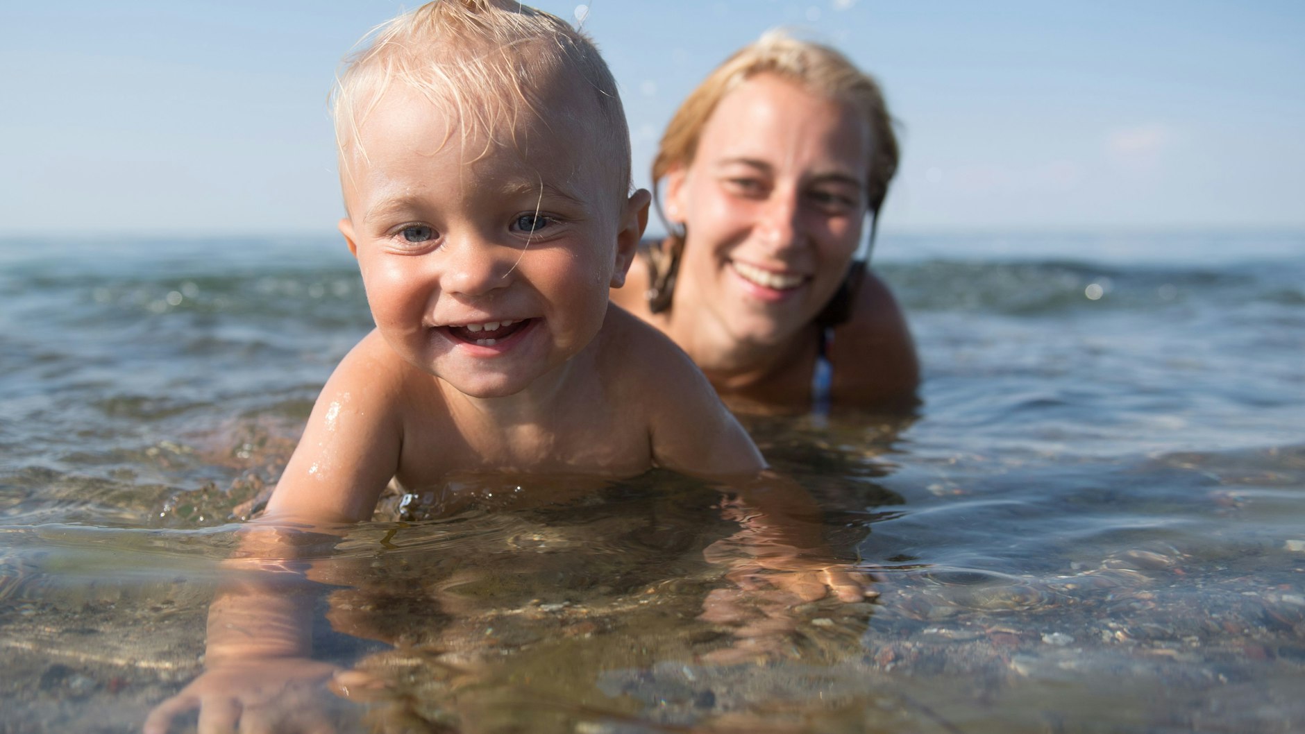 Eltern sollten schon früh dafür sorgen, dass ihre Kinder Spaß am Wasser haben. Dieser kleine Junge planscht vergnügt am Ufer. Seine Mama bleibt konsequent in Griffweite – so kann sie zupacken, falls etwas passiert.&nbsp;