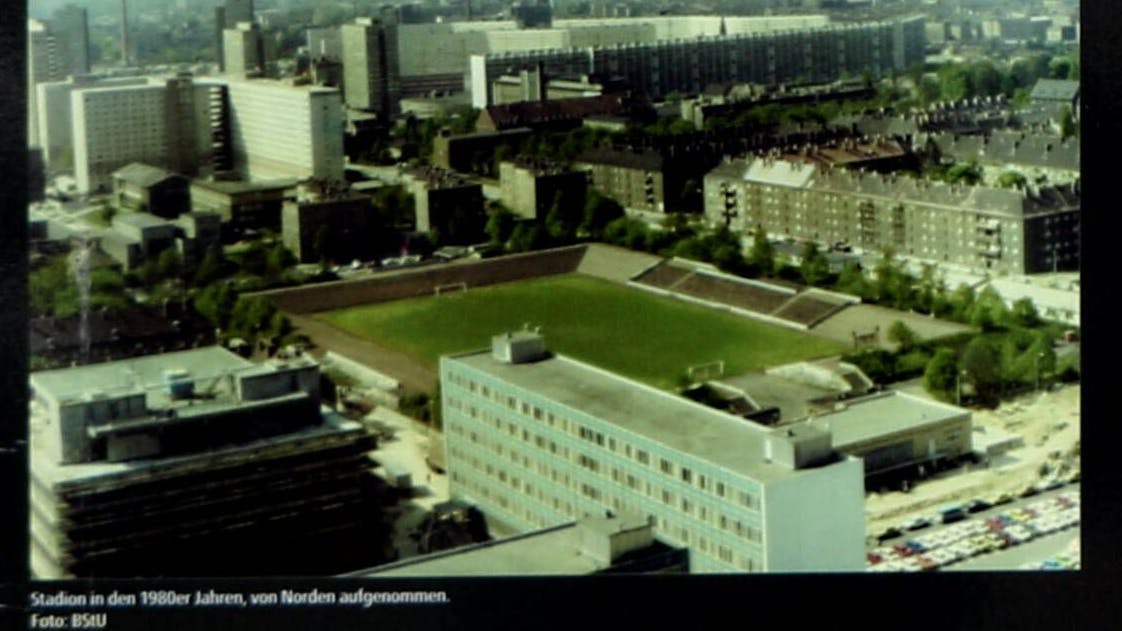 Das Hans-Zoschke-Stadion: Das Foto, das auf einer Erinnerungstafel am heutigen Stadion zu sehen ist, wurde in den 80ern von der Stasi aufgenommen. Hinter der Arena grenzt die Zentrale des Ministerium für Staatssicherheit.