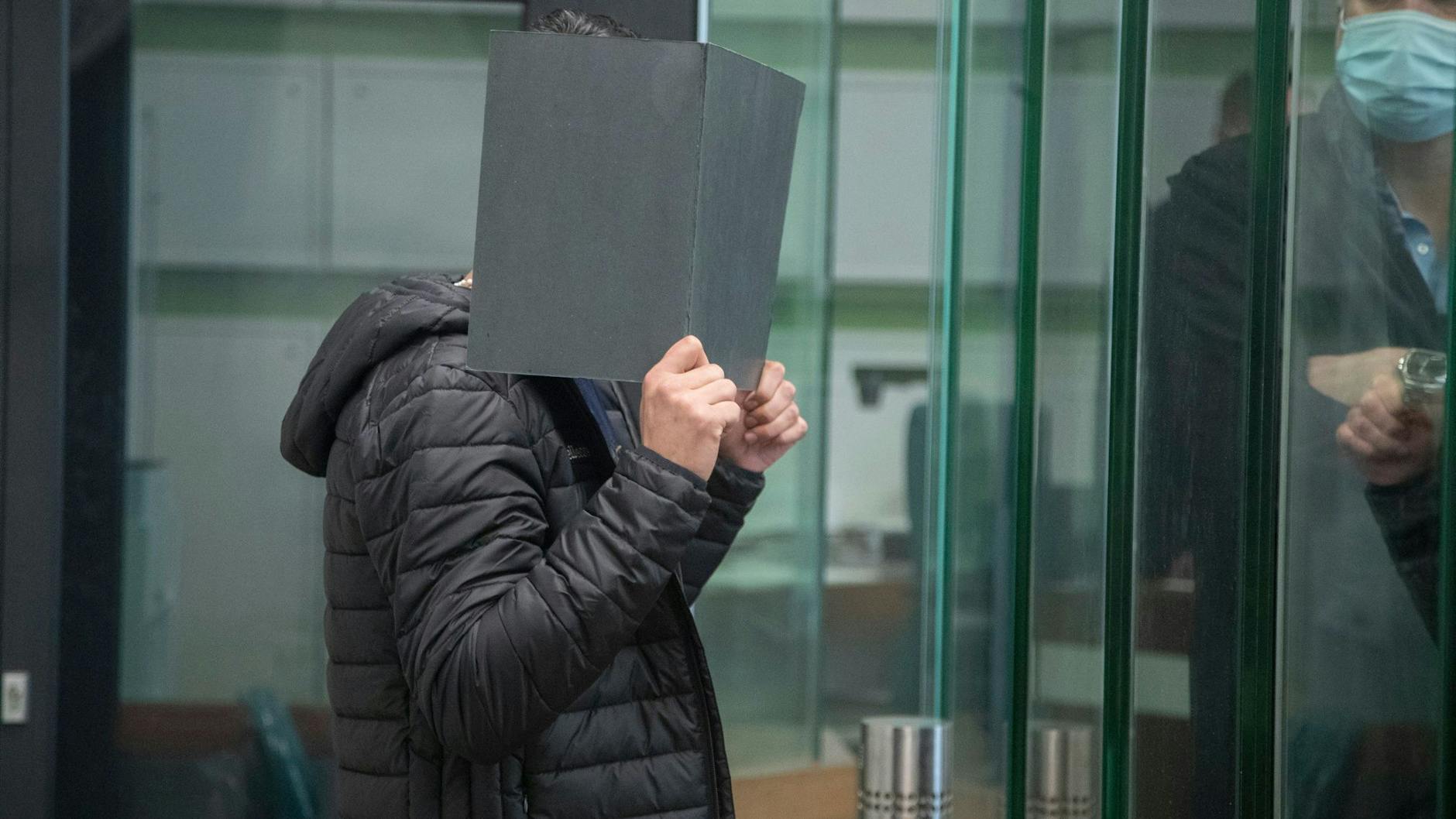 Vor Gericht: Einer der Angeklagten versteckt sein Gesicht hinter einem Aktenordner.