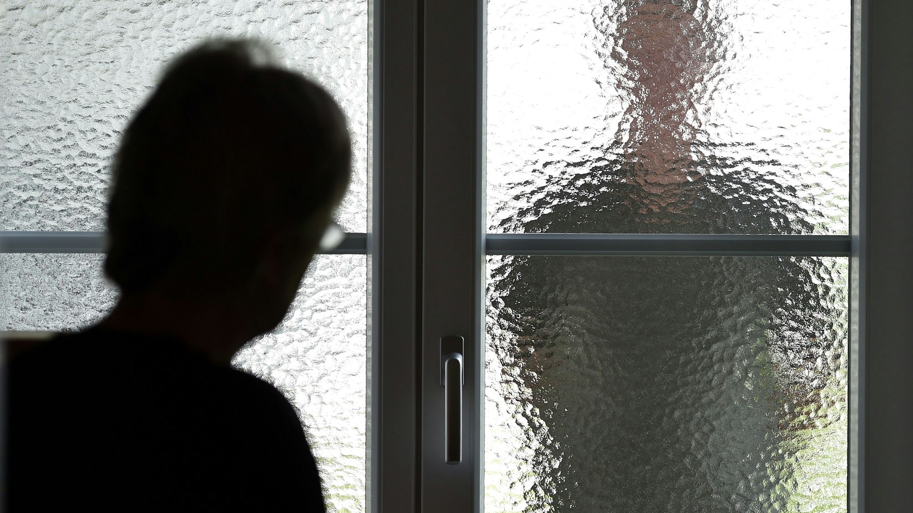 Eine Frau steht an einer Glasscheibe, hinter der ein Stalker wartet.&nbsp;