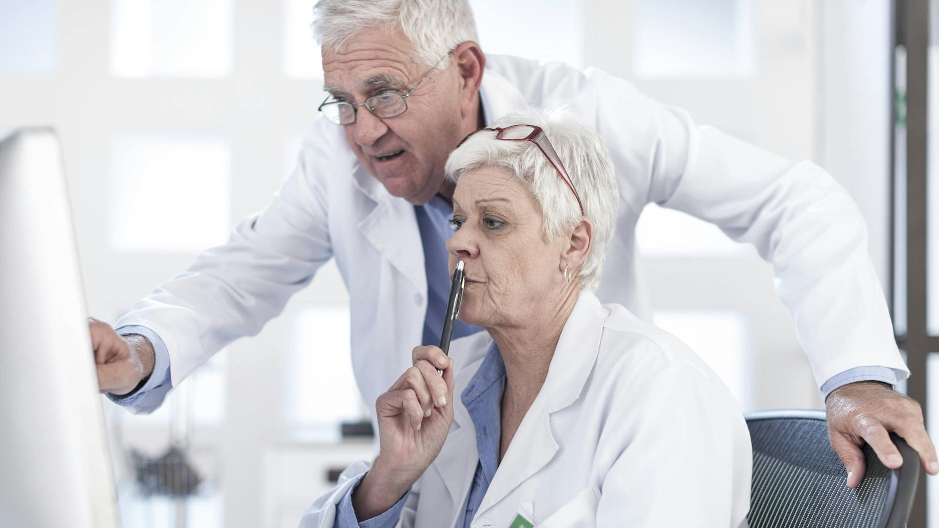 Eine Ärztin und ein Arzt studieren eine Patientenakte am Computer.