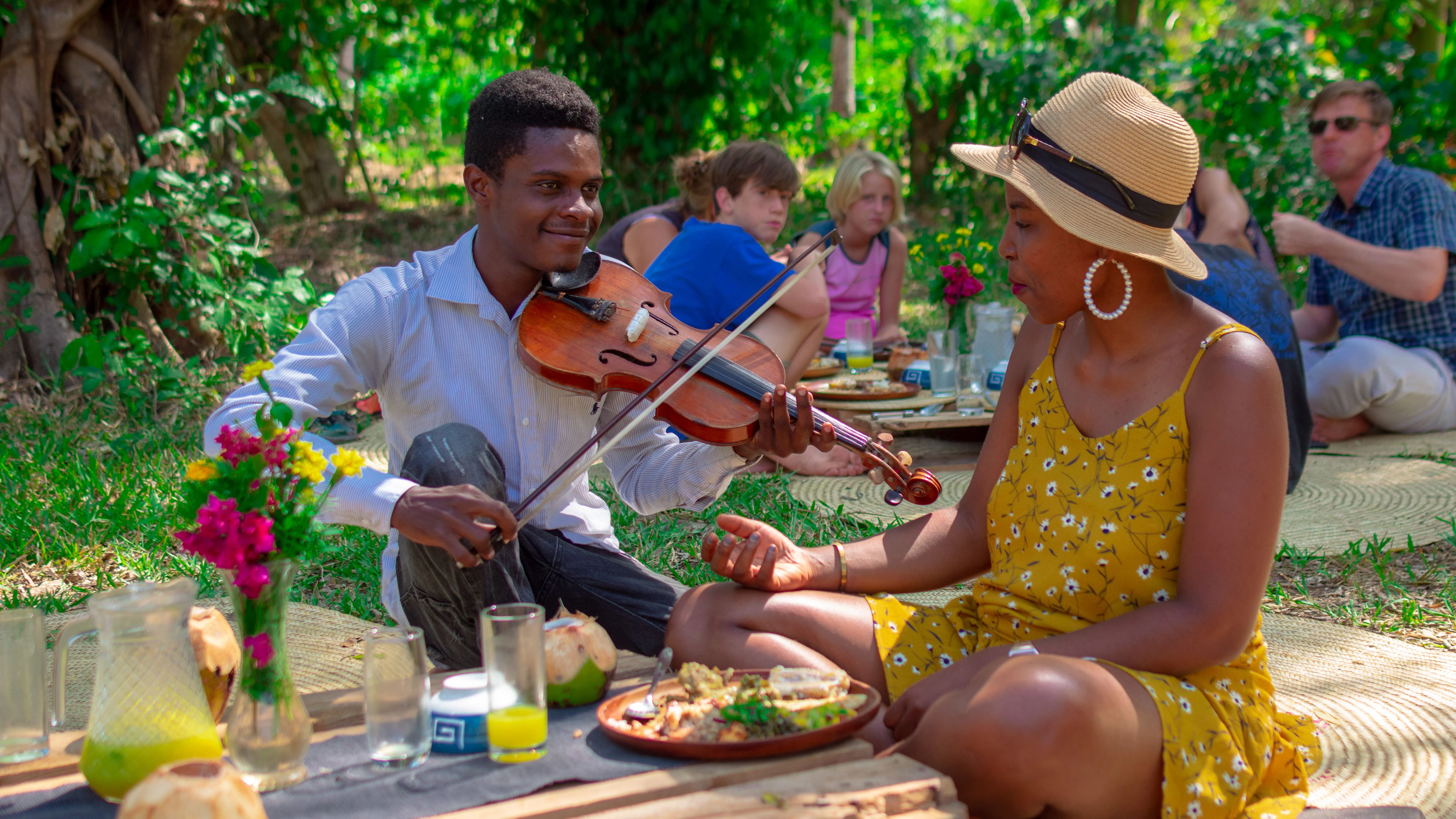 Ein Geiger spielt einer Touristin bei einem Picknick auf einer Öko-Farm ein Lied vor.
