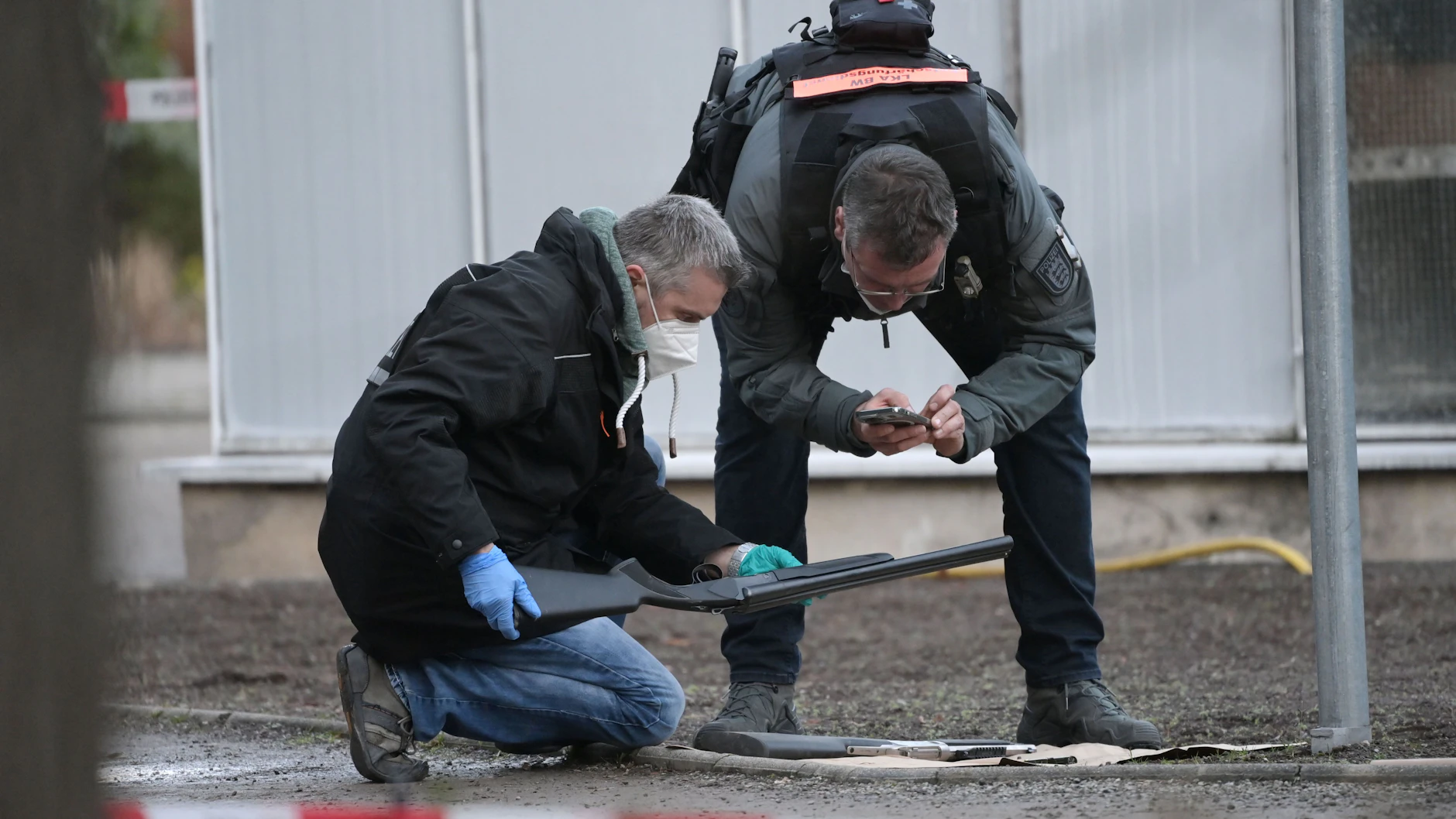  Polizeibeamte mit zwei Waffen des Amokschützen. Eine ist eine doppelläufige Schrotflinte, die andere ein Repetiergewehr. 