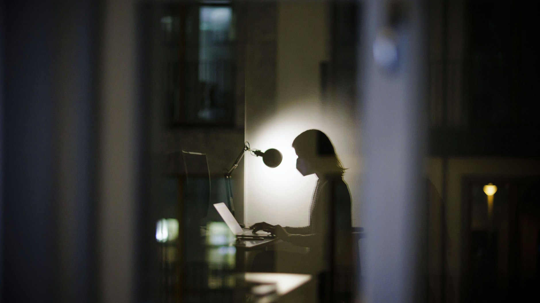 Eine Frau sitzt abends mit Maske an in ihrem Schreibtisch.