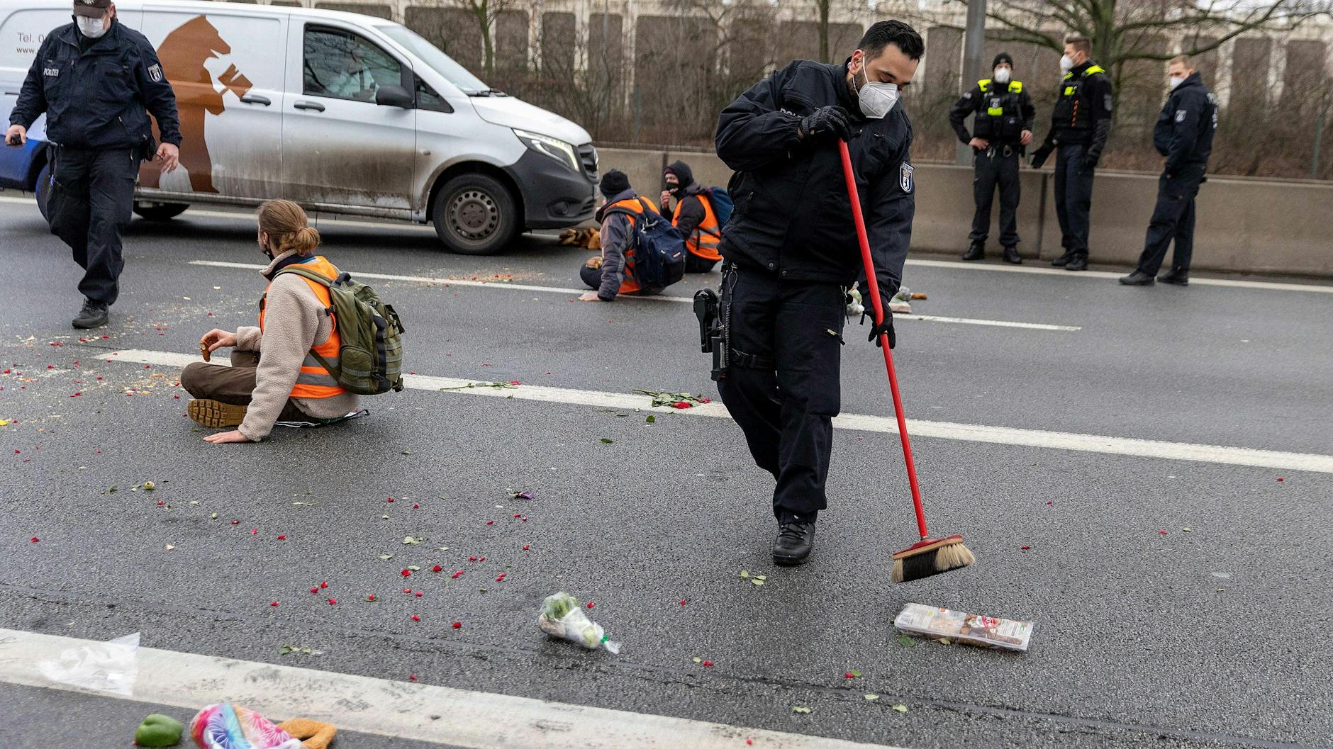 Ein Polizist fegt mit Lebensmittel von der Straße, während Klimaaktivisten auf der Fahrbahn vor der Ausfahrt Beusselstraße gegen Lebensmittelverschwendung protestieren.