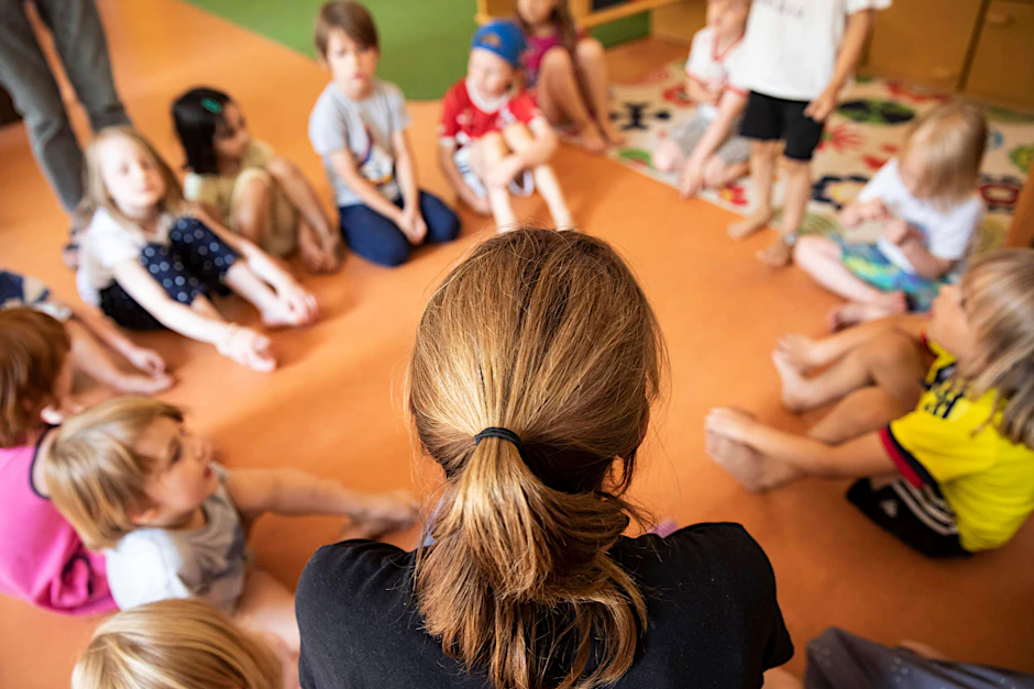 Eine Erzieherin sitzt mit ihren Kindern im Morgenkreis.