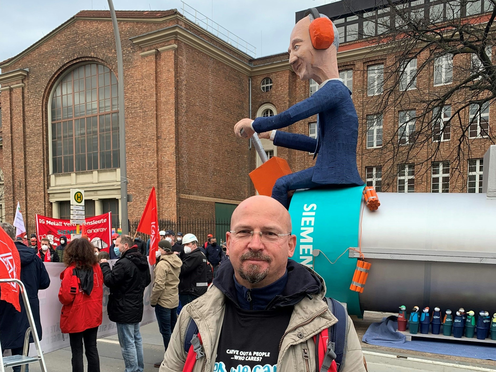 Matthias Reifenberger, Vertrauensmann der IG Metall im Dynamowerk. Hinter ihm die Puppe des Siemens-Chefs, der auf einem Elektromotor hockt und dabei ist,&nbsp; Motor,&nbsp; Mitarbeiter und sich in die Luft zu sprengen.