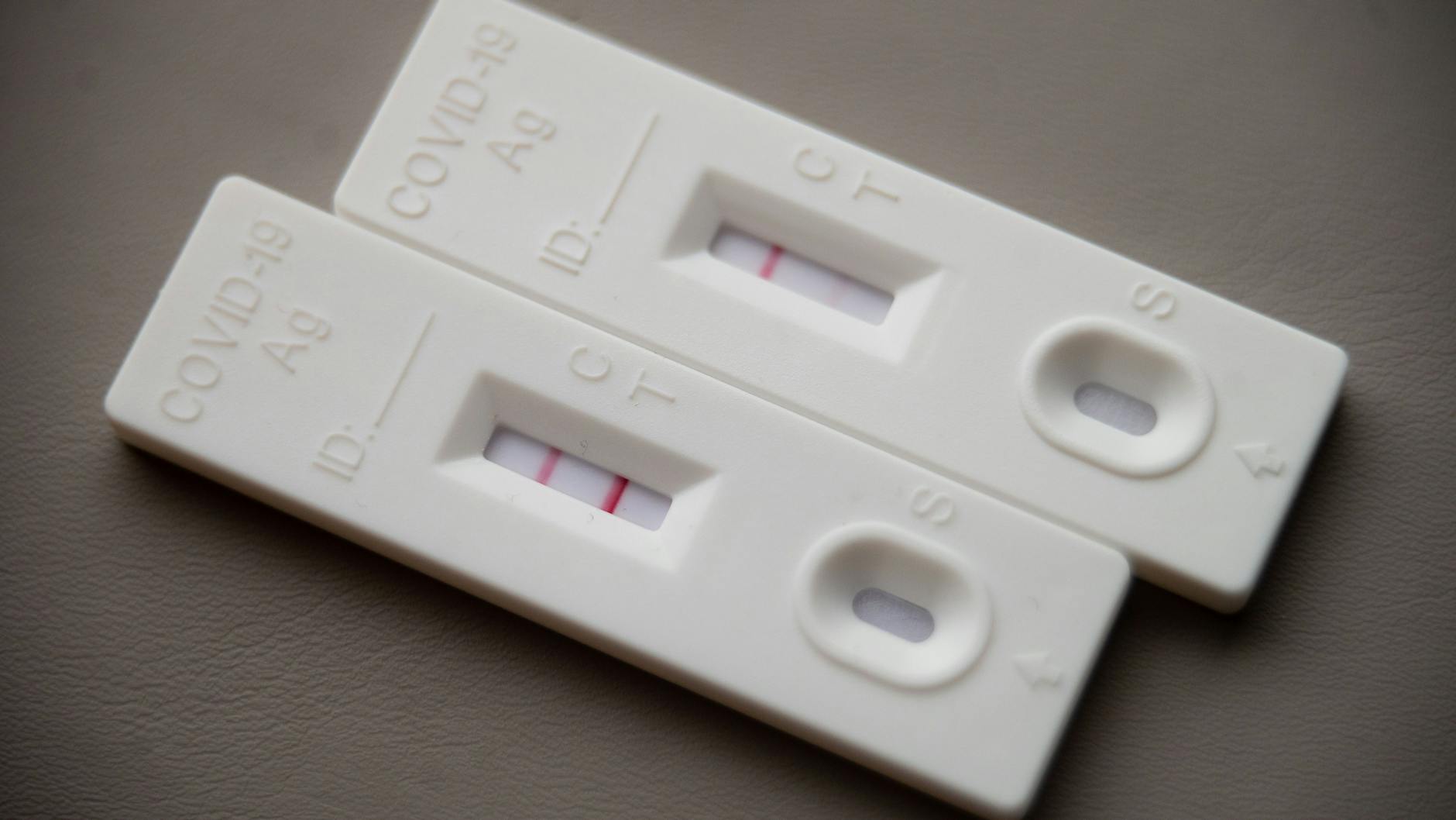Ein positiver Corona-Selbsttest liegt auf einem Tisch neben einem Corona-Schnelltest, der eine schwach positive Linie hat.