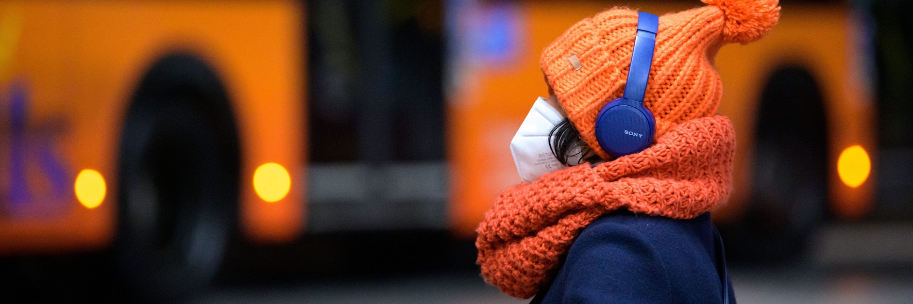 Eine Frau sitzt mit FFP2-Maske an einem Busbahnhof. Die Maskenpflicht soll uns noch eine Weile erhalten bleiben. Viele andere Maßnahmen werden gelockert oder abgeschafft.