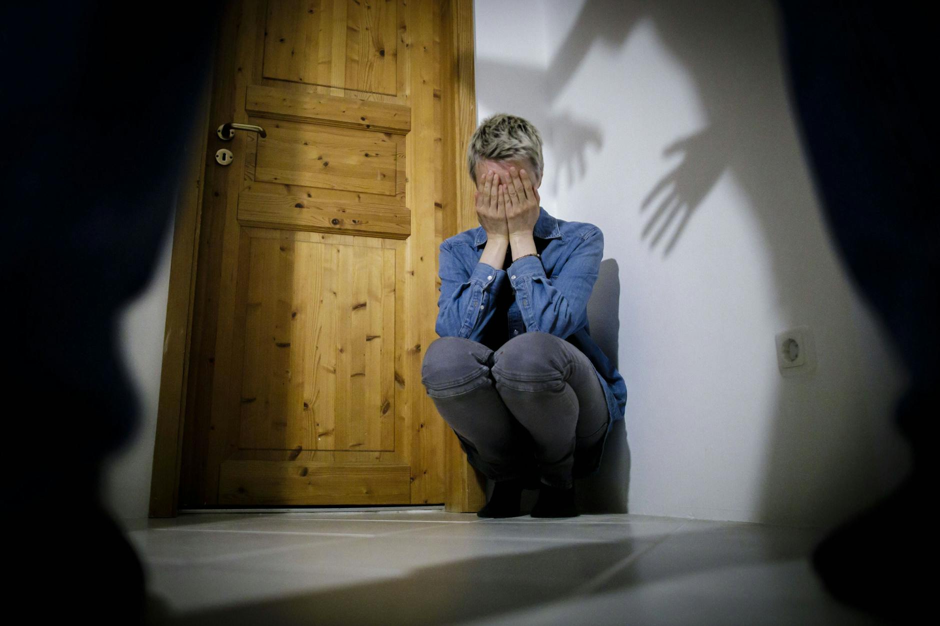 Eine junge Frau sitzt auf dem Boden und hält sich schützend die Hände vor ihr Gesicht.