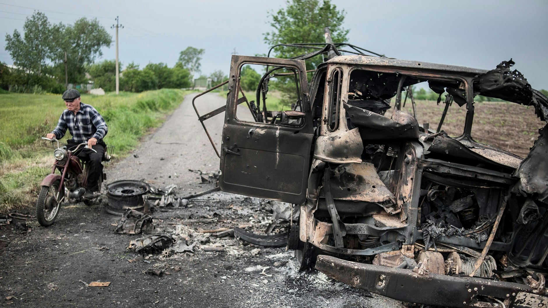 Ein Mann fährt im Mai 2014 auf seinem Motorrad an einem verbrannten ukrainischen Militärfahrzeug im Dorf Oktyabrskoe in der Nähe der ostukrainischen Stadt Kramatorsk vorbei.