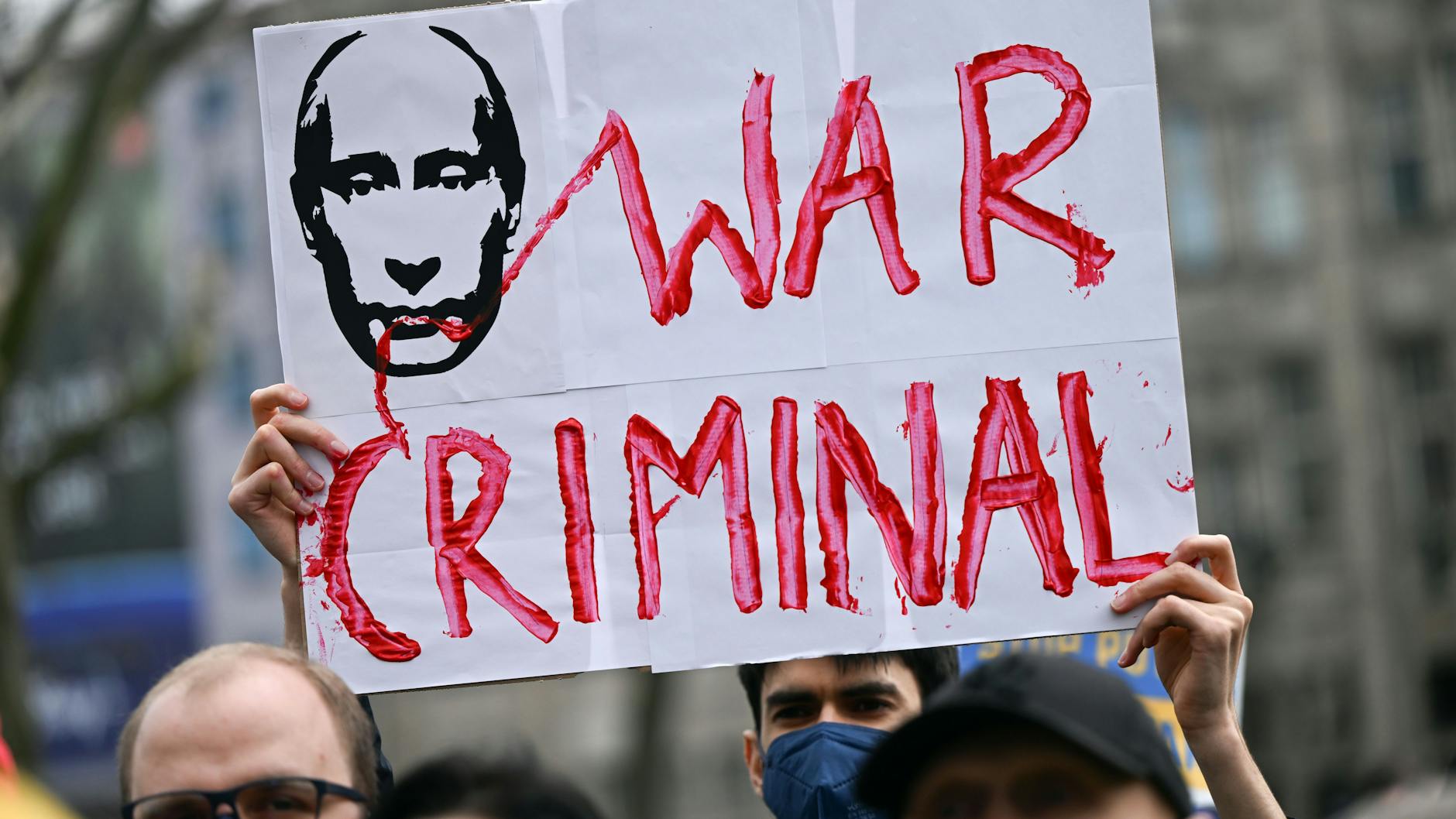 Ein Demonstrant in Köln hält ein Plakat mit dem Konterfei des russischen Präsidenten Putin und der Aufschrift „War Criminal“ („Kriegsverbrecher“) in den Händen.