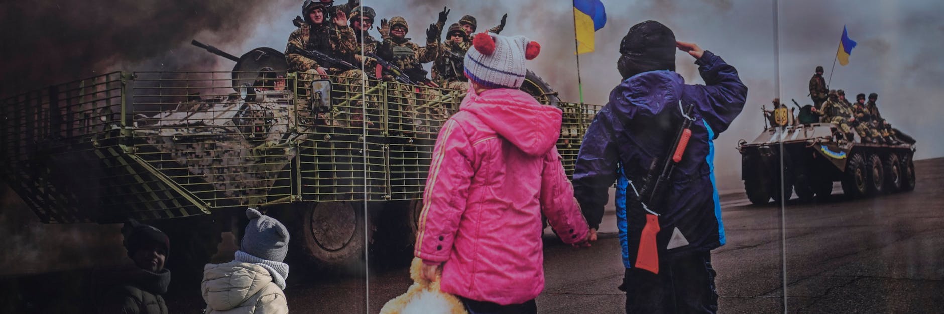 Ukrainische Kinder gehen an einem großformatigen Bild, aufgestellt im Gedenken an die ukrainischen Toten der Konfrontation zwischen dem ukrainischen Militär und den prorussischen Separatisten, vorbei. Wie erklärt man Kindern in Deutschland den Krieg?