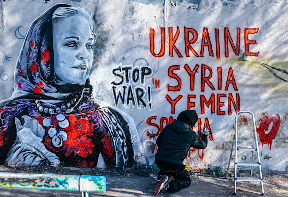 Eine Streetart-Künstlerin vollendet ihr Bild gegen den Krieg in der Ukraine an einer Berliner Mauer.