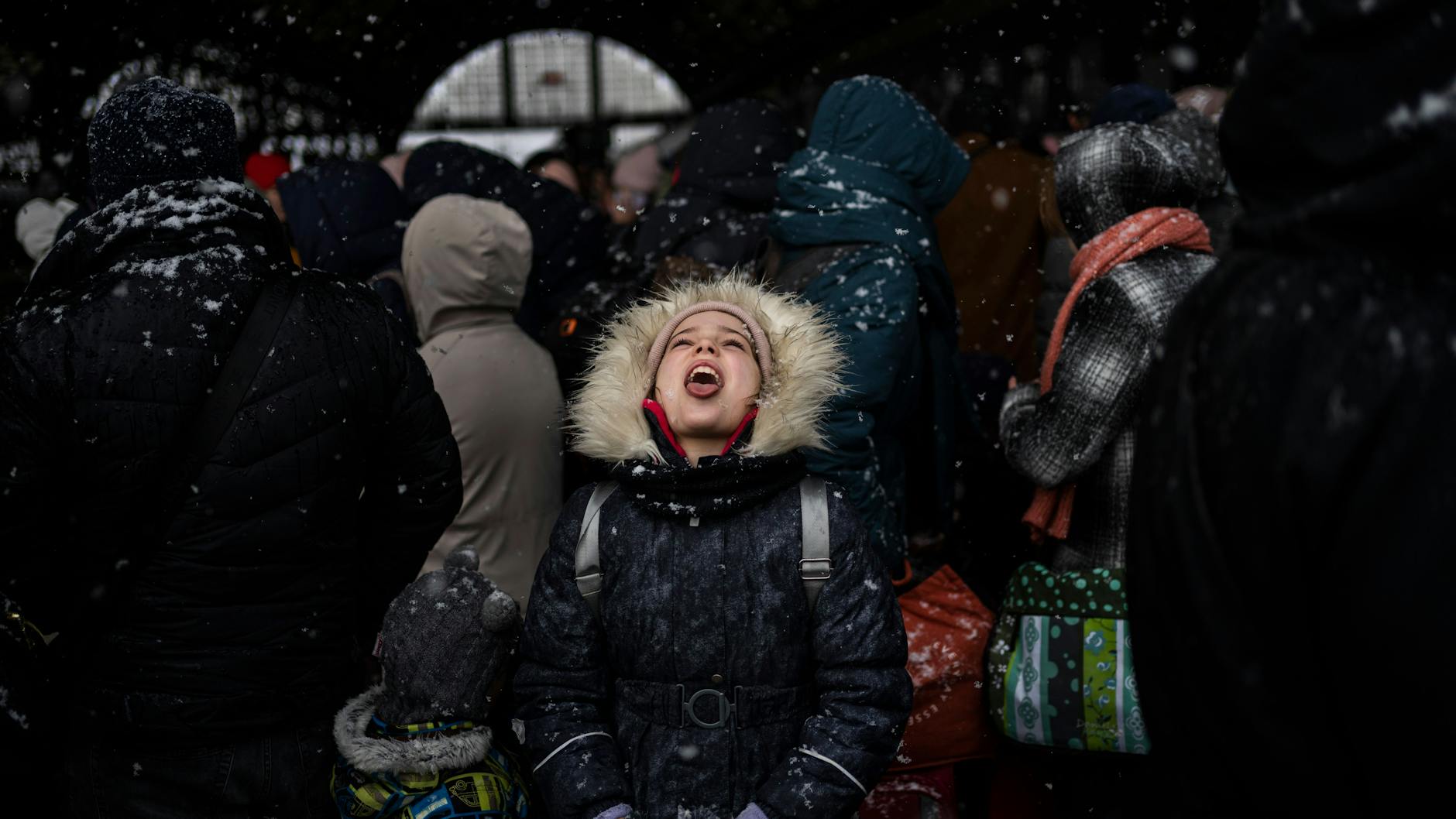 Ein kleines Mädchen fängt mit ihrem Mund eine Schneeflocke auf, während sie mit Hunderten Menschen am Bahnhof von Lwiw auf einen Zug nach Polen wartet.