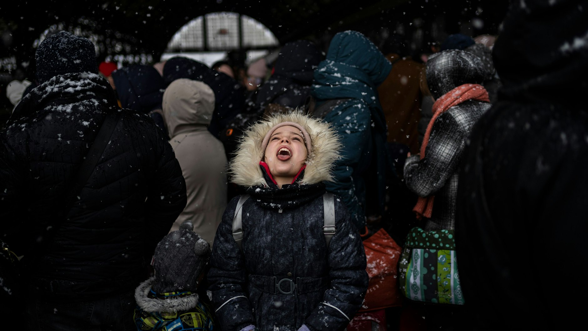 Ein kleines Mädchen fängt mit ihrem Mund eine Schneeflocke auf, während sie mit Hunderten Menschen am Bahnhof von Lwiw auf einen Zug nach Polen wartet.