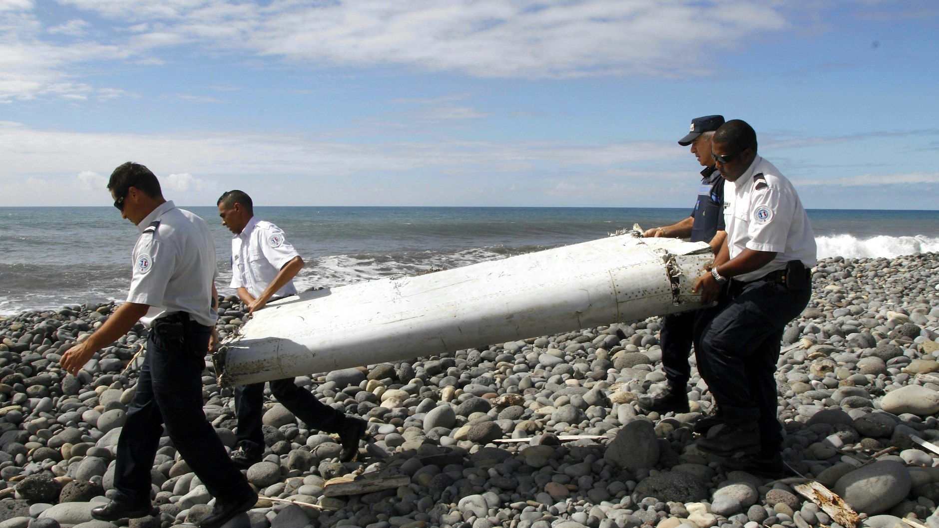 Techniker tragen ein Wrackteil, die Flügelklappe eines Flugzeugs, über einen Strand bei Saint-Andre de la Reunion. Vor acht Jahren verschwand eine Boeing, mit ihr 239 Menschen an Bord. 