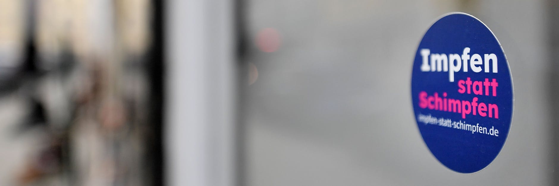 „Impfen statt Schimpfen“ steht auf dem kleinen Aufkleber an der Fensterscheibe eines Geschäfts (Symbolbild).