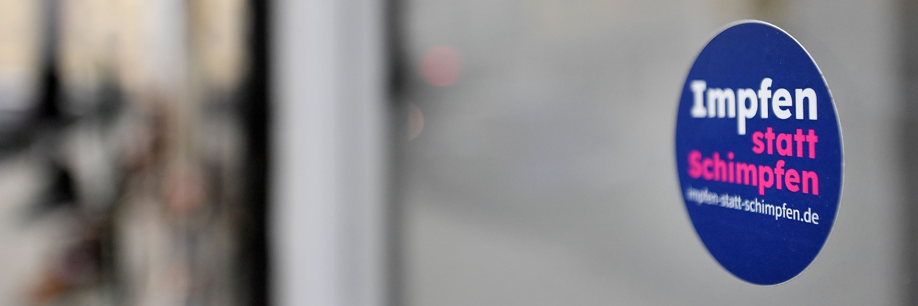 „Impfen statt Schimpfen“ steht auf dem kleinen Aufkleber an der Fensterscheibe eines Geschäfts (Symbolbild).