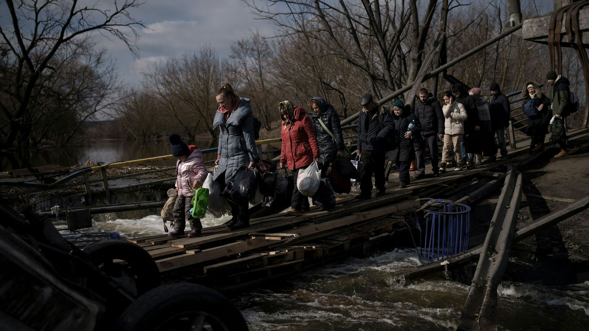 Ukrainer überqueren einen improvisierten Weg unter einer zerstörten Brücke auf der Flucht vor russsischen Angriffen aus Irpin, am Stadtrand von Kiew, Ukraine.