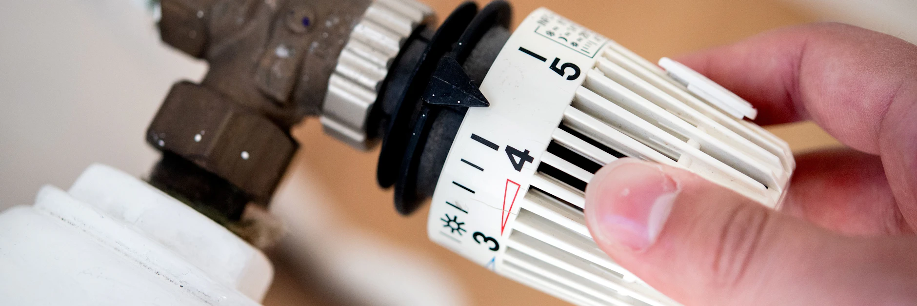 Ein Mann dreht in einer Wohnung am Thermostat einer Heizung.