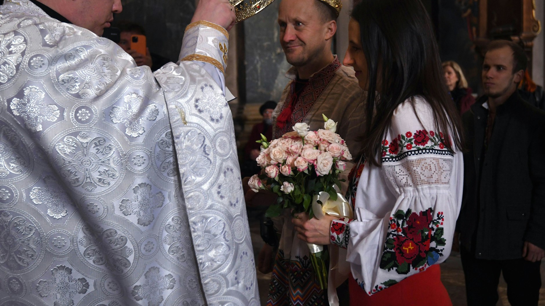 Wladimir Ozarkow (M) und Ulyana Kudla (r.) heiraten in der in der Kirche der heiligen Apostel Peter und Paul während der russischen Invasion in der Ukraine. Das Ehepaar hat ihre Hochzeit vorverlegt, da Wladimir Ozarkow eingezogen wurde und sich am nächsten Tag zum Einsatz melden muss.