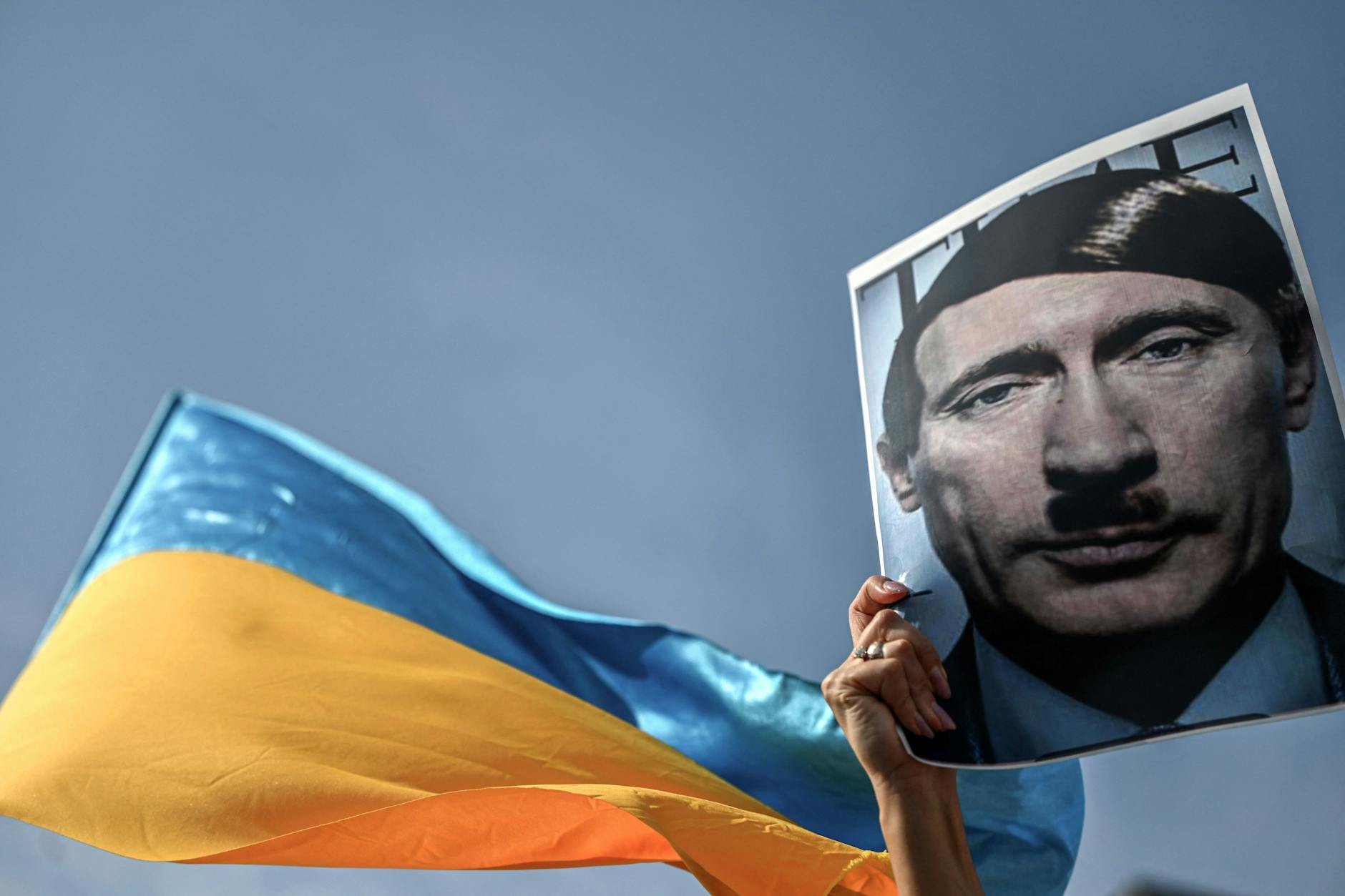 Eine Demonstrantin hält ein Bild, das den russischen Präsidenten Wladimir Putin als Adolf Hitler zeigt.