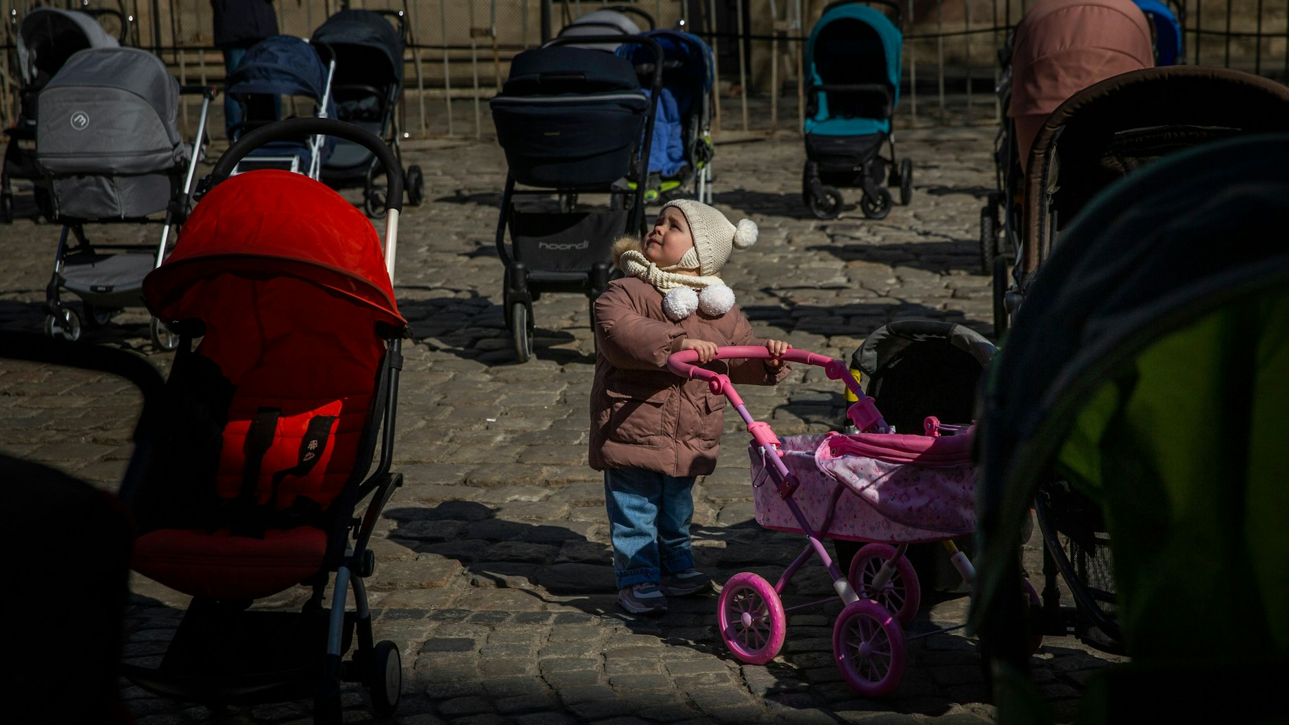 Die kleine Emilia (2) steht zwischen den leeren Kinderwagen. Sie sollen der Welt zeigen, wie eine Flugverbotszone Leben retten könnte.