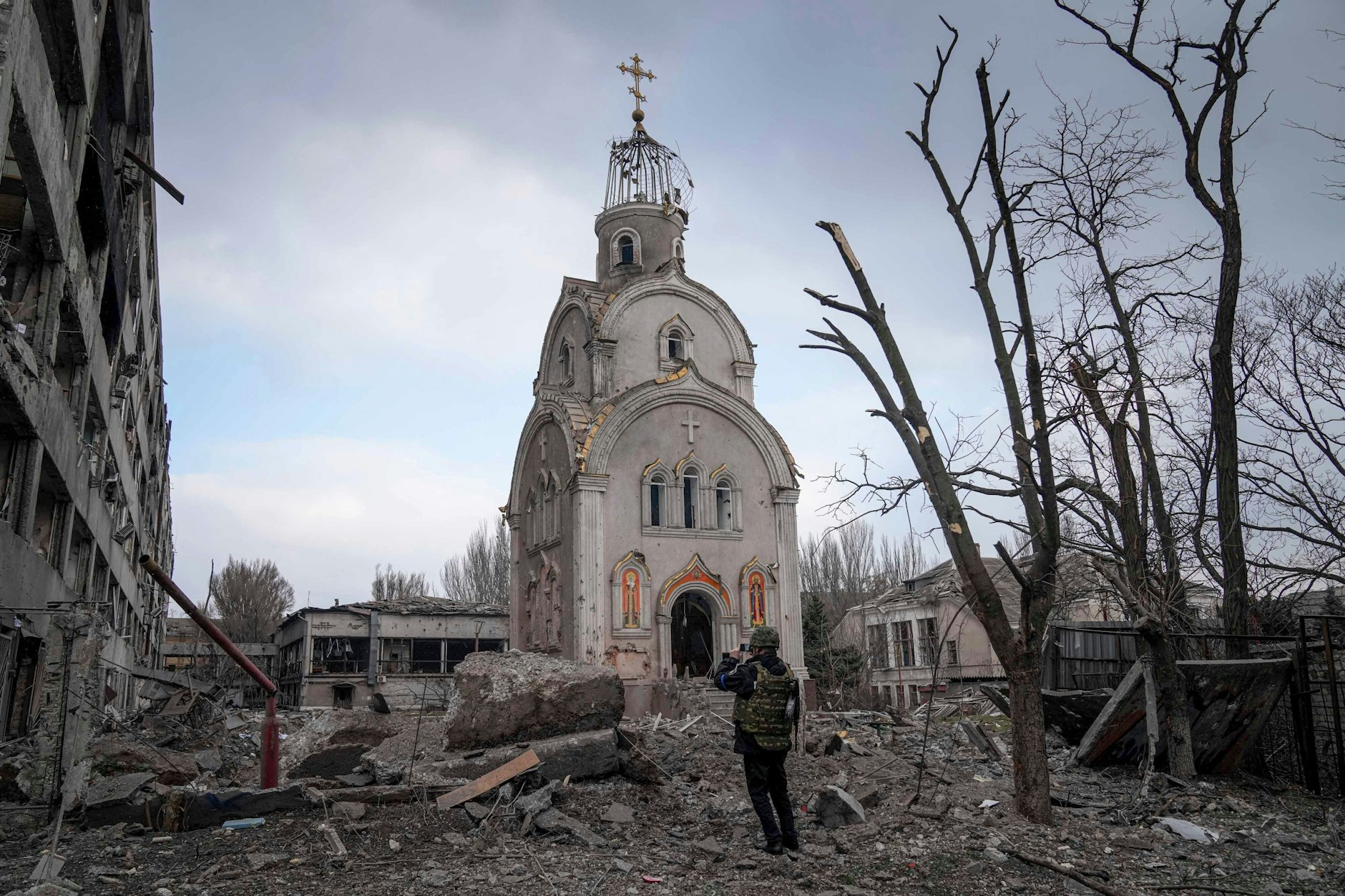 Ein Soldat steht neben einem zerschossenen Wohnhaus vor einer beschädigten Kirche in Mariupol.