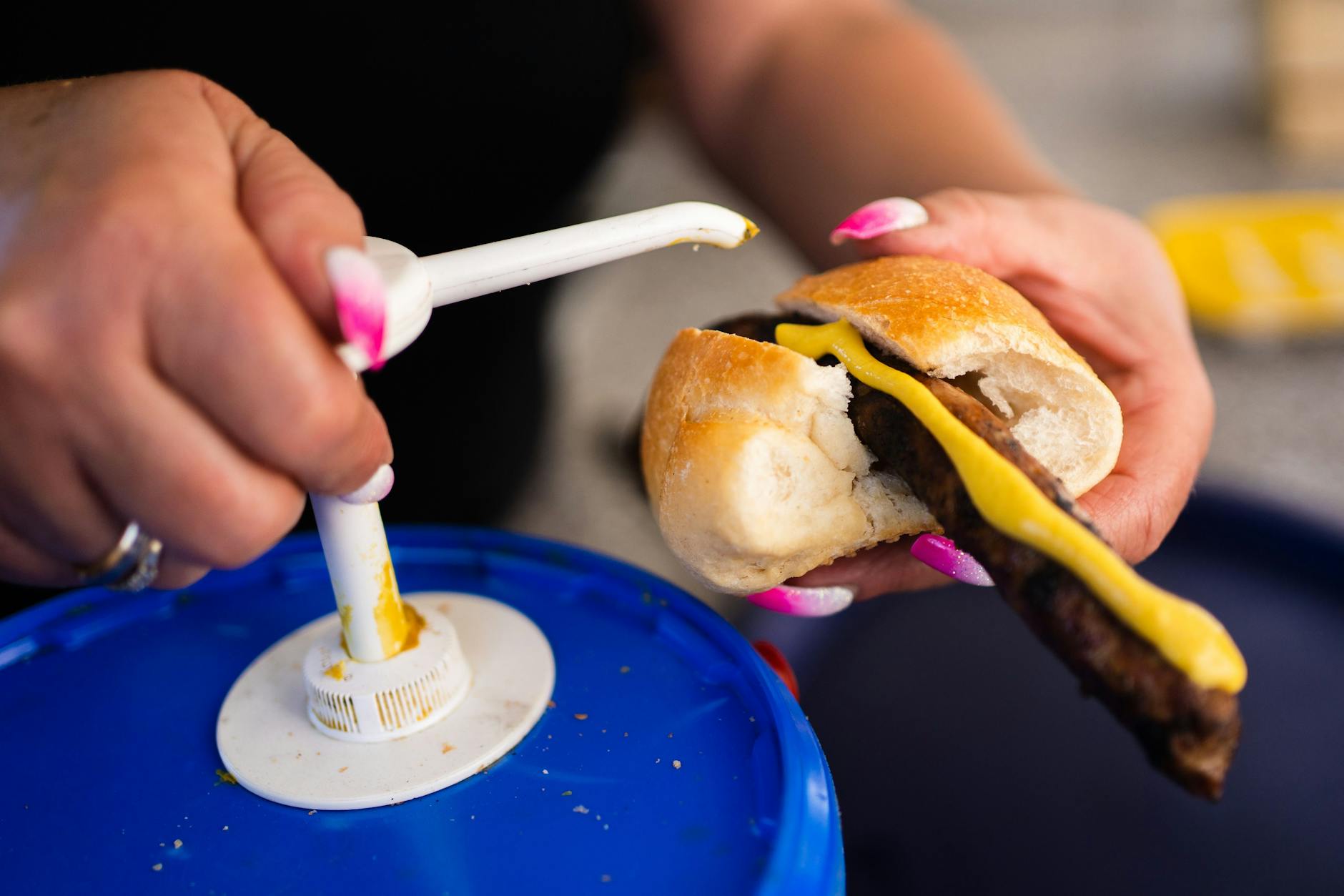 Eine Frau gibt Senf auf eine Bratwurst. In Deutschland könnte Senf wegen Engpässen beim Saatgut deutlich teurer werden.