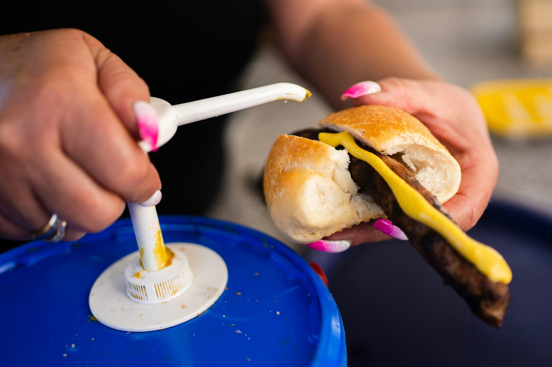 Eine Frau gibt Senf auf eine Bratwurst. In Deutschland könnte Senf wegen Engpässen beim Saatgut deutlich teurer werden.