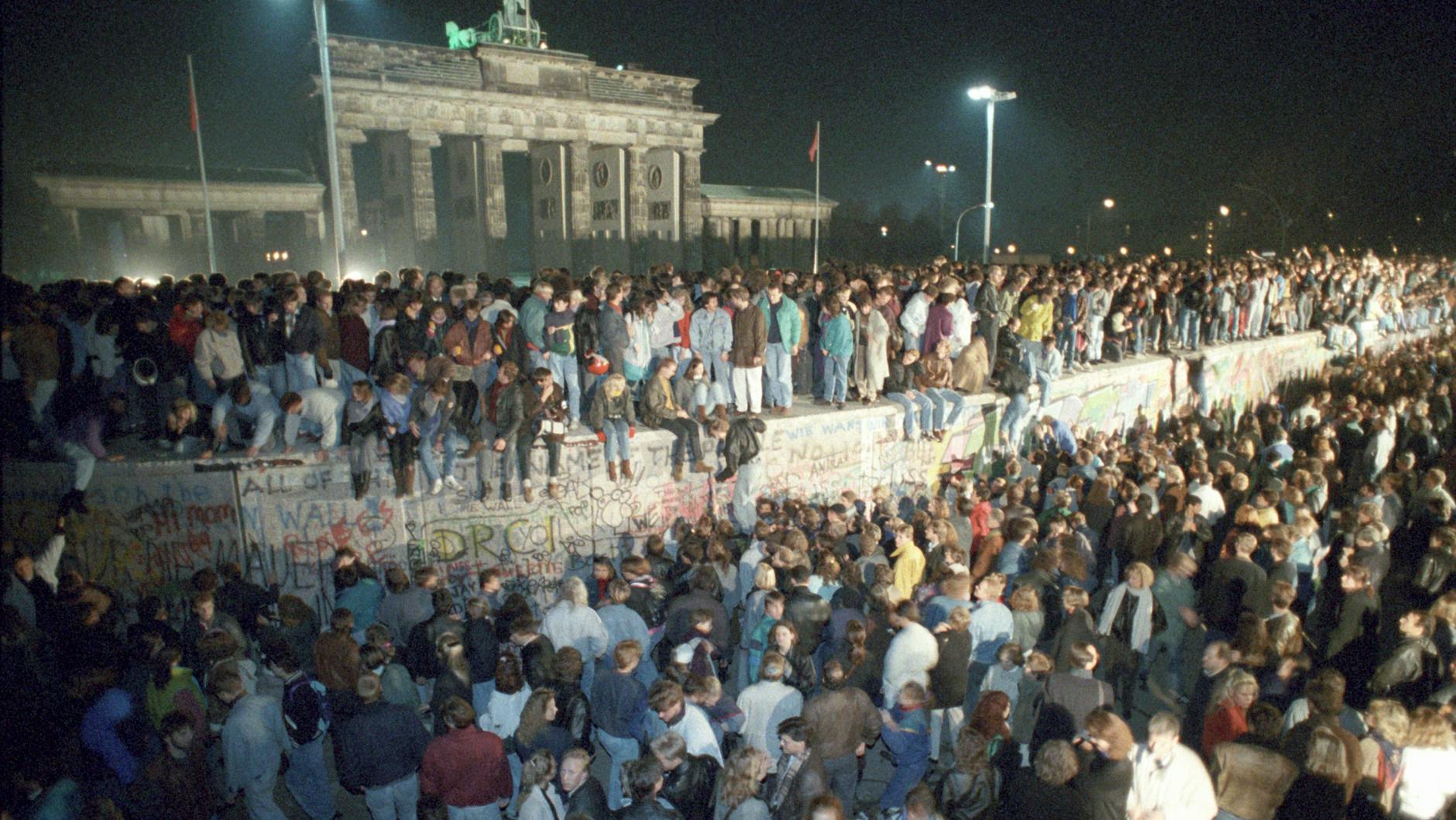 Menschen auf der Berliner Mauer vor dem Brandenburger Tor in der Nacht vom 9. auf den 10. November 1989. 