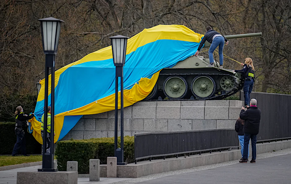 Polizisten entfernen eine der riesigen ukrainischen Fahnen, die über die beiden sowjetischen Panzer am Ehrenmal in Tiergarten gelegt worden waren.