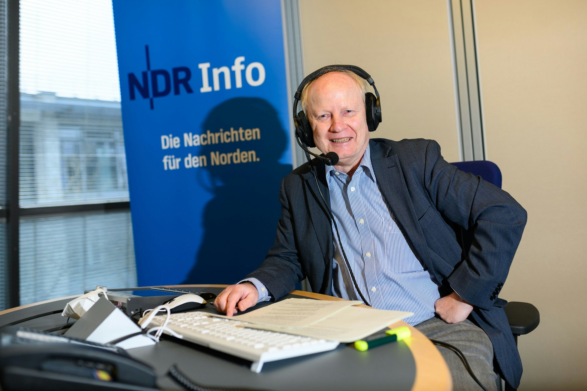 NDR-Sicherheitspolitikexperte Andreas Flocken spricht in einem Aufnahmestudio vor dem Logo des Nachrichtenformats. Seinen Podcast "Streitkräfte und Strategien" wollen viele Menschen hören.