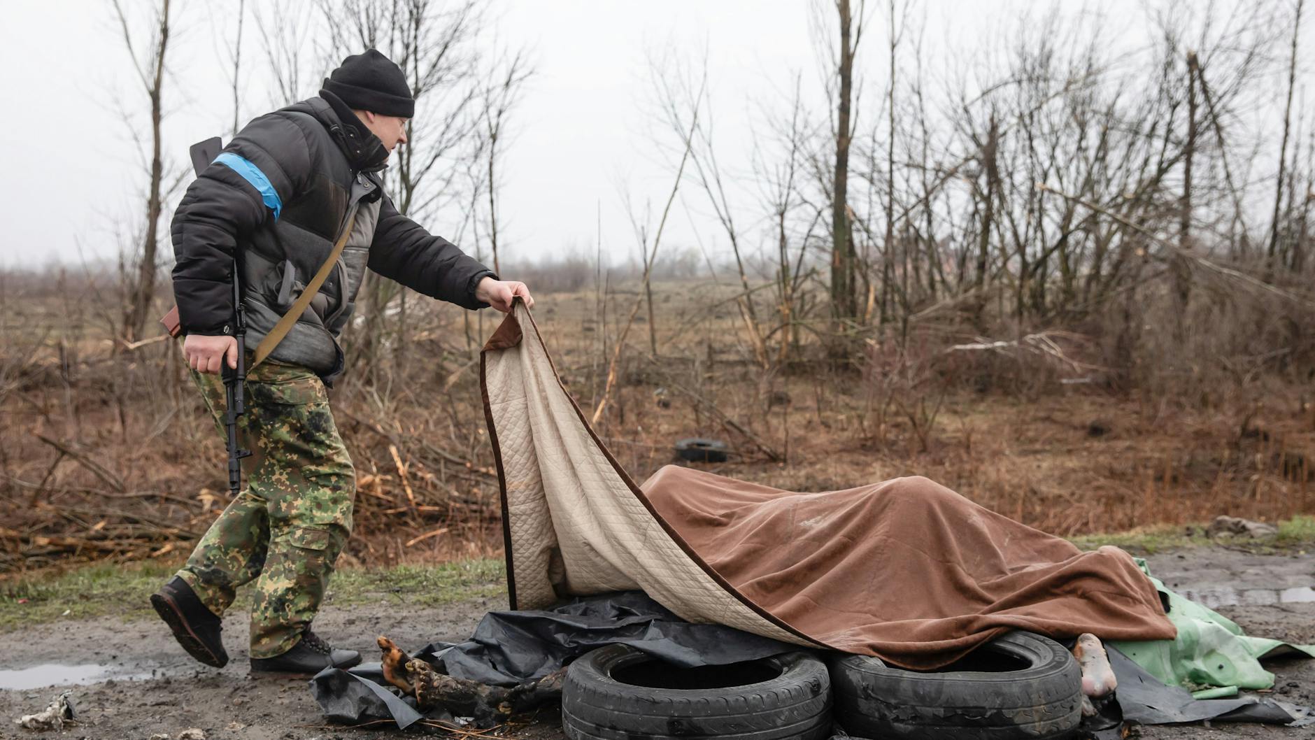 Ein Mitglied der zivilen Schutztruppe deckt betrachtet unter einer Decke am Rande der Autobahn, 20 km von Kiew entfernt, vier tote Zivilisten. Fast 300 Zivilisten wurden entlang der Straße zwischen Zhytomyr und Kiew in der Nähe von Butscha getötet. Die meisten Opfer versuchten, den Fluss Buchanka zu überqueren, um das ukrainisch kontrollierte Gebiet zu erreichen, und wurden dabei getötet.