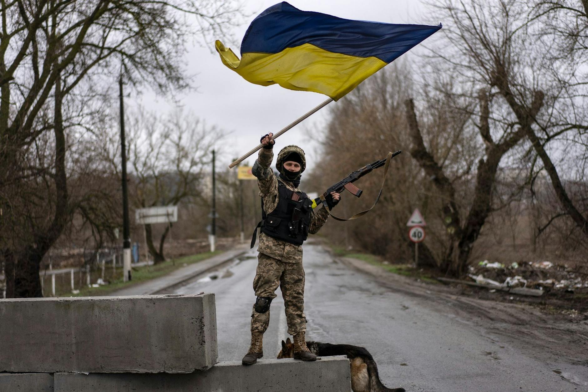 Butscha: Ein ukrainischer Soldat steht an einer Straßenblockade und hält die ukrainische Flagge hoch.