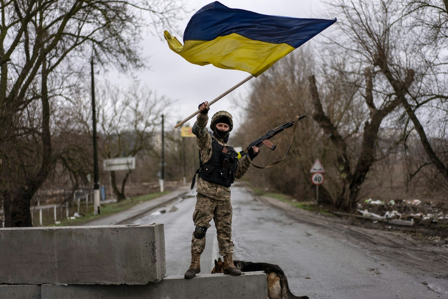 Butscha: Ein ukrainischer Soldat steht an einer Straßenblockade und hält die ukrainische Flagge hoch.