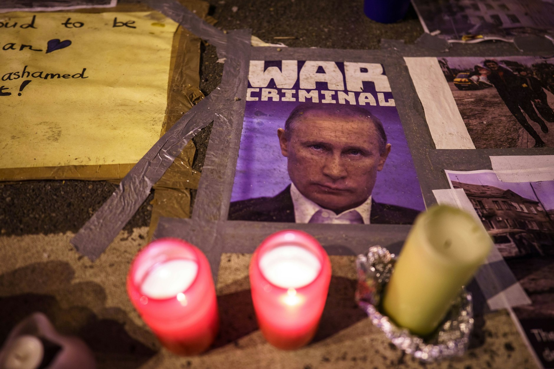 Kerzen brennen vor einem Bild des russischen Präsidenten Putin, das ihn als „War Criminal“ (Kriegsverbrecher) bezeichnet.