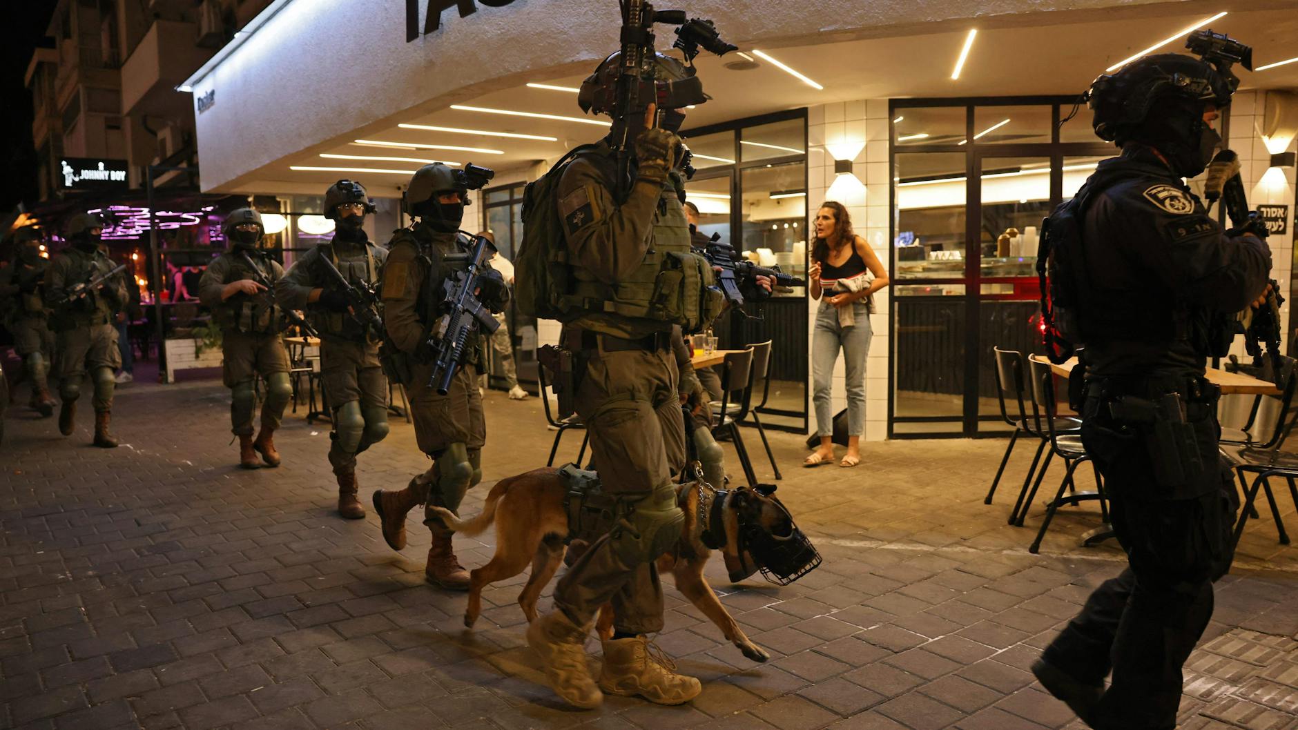 Mitglied der Sicherheitskräfte gehen mit einem Polizeihund vor einem Restaurant am Tatort eines Schussangriffs in Tel Aviv lang. Mindestens zwei Menschen wurden getötet und mehrere verletzt.