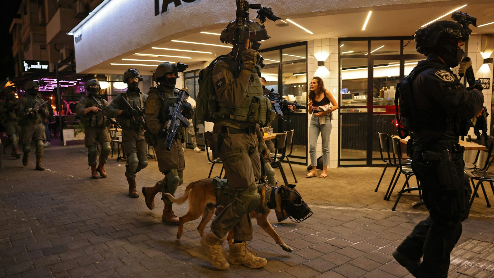 Mitglied der Sicherheitskräfte gehen mit einem Polizeihund vor einem Restaurant am Tatort eines Schussangriffs in Tel Aviv lang. Mindestens zwei Menschen wurden getötet und mehrere verletzt.