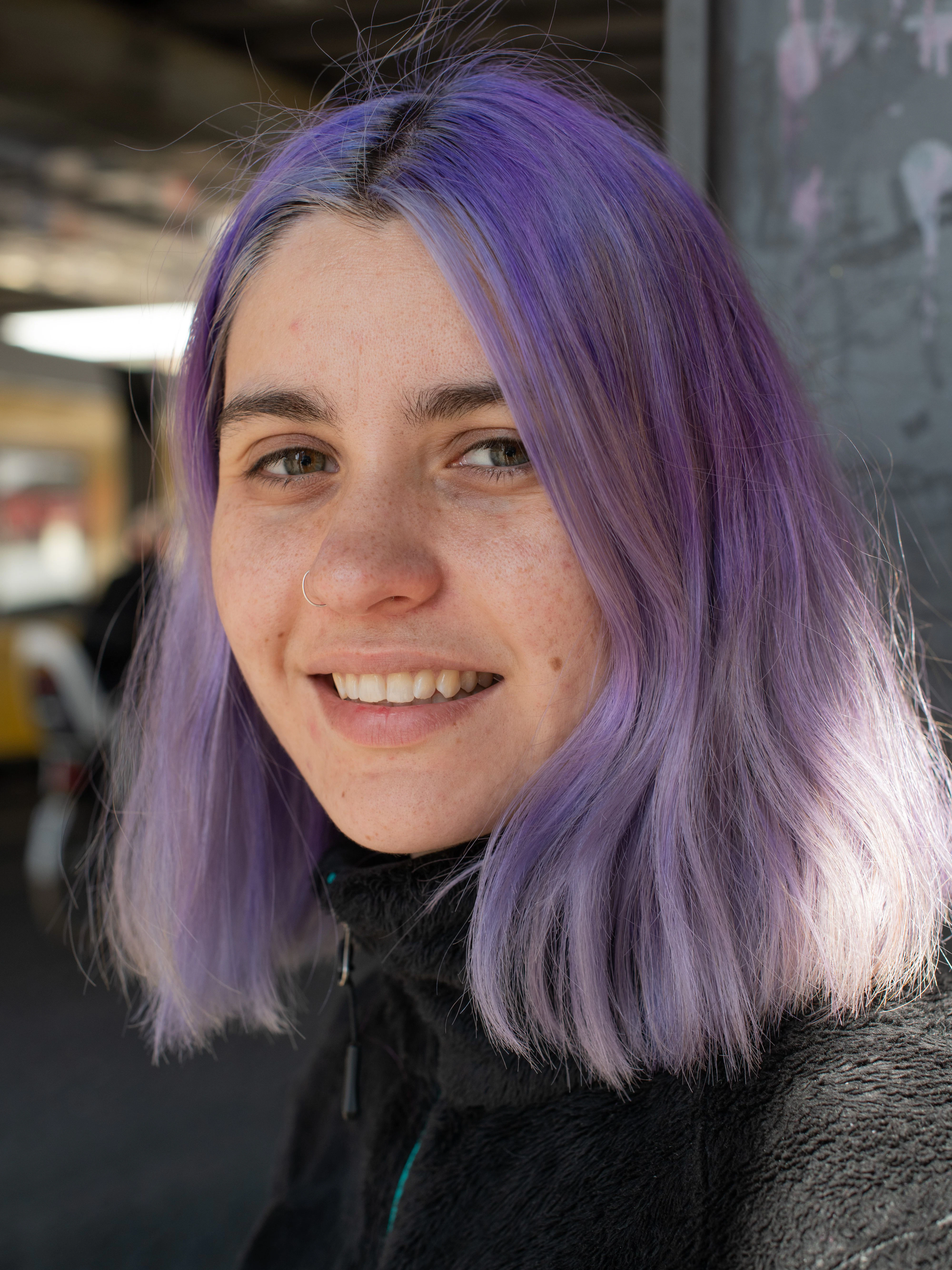 Raxide trägt gerne knallige Farben auf dem Kopf. Derzeit ist es ein pastelliges Violett. Dazu kombiniert sie ein schlichtes Outfit in Schwarz, bestehend aus Teddy-Jacke von The North Face, Uniqlo-Hose und Reebok-Sneakers. Dazu eine Crossbody-Bag der Outdoor-Marke Patagonia.