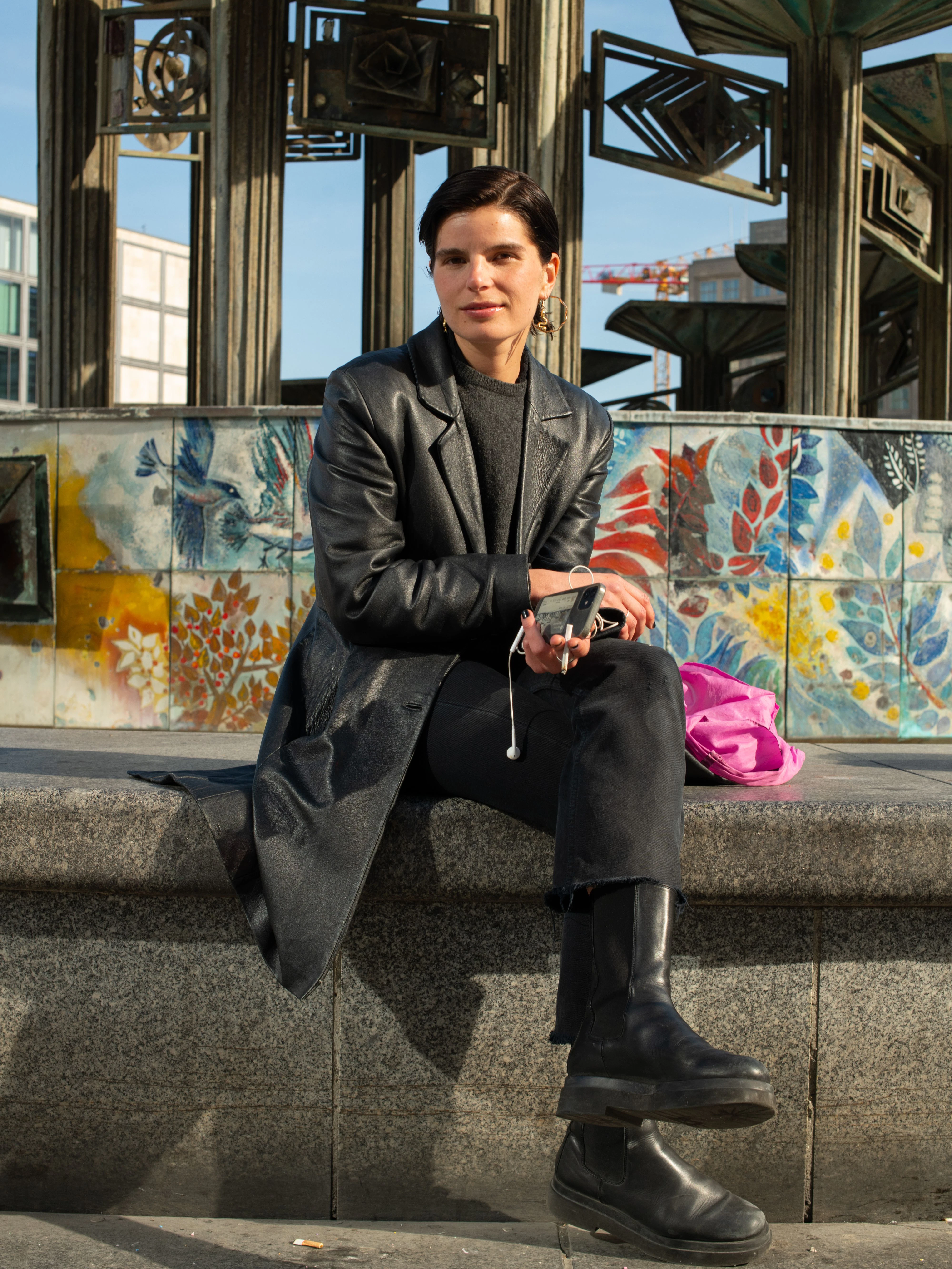 Großstadtromantik pur: Julie wartet am Brunnen der Völkerfreundschaft auf ihren Freund. Sie arbeitet als freischaffende Künstlerin, derzeit vor allem als Set-Designerin für Musikvideos. Sie kauft eigentlich alles nur „Vintage“, sagt sie, außer den Schuhen, die von Högl sind. Den Ledermantel hat sie auf einem Pariser Flohmarkt erstanden, die schwarze Levi
