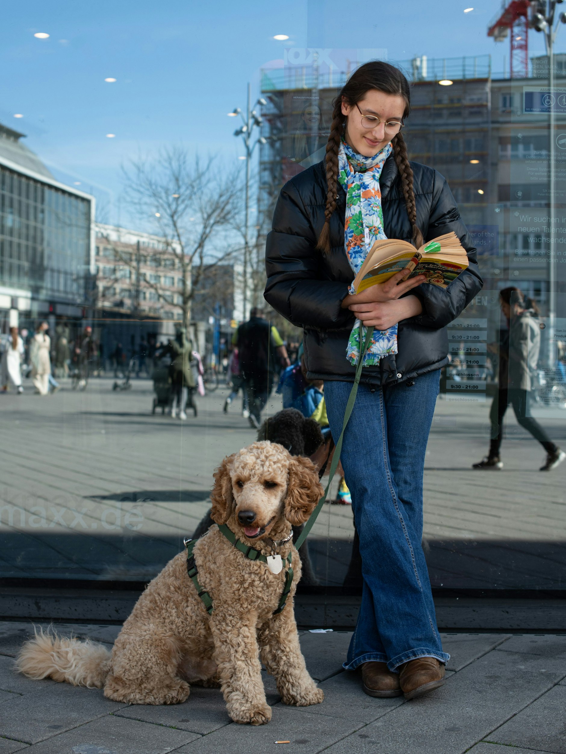 Man sagt, das Bücherlesen sei zurück. Hier ein wunderschöner Beweis in Person von Nona aus Prenzlauer Berg. Sie und ihr Goldendoodle Buba warten auf Mama, die gerade einkaufen ist. Nona trägt eine Pufferjacke von Hallhuber, Tuch und Jeans sind von Mango.