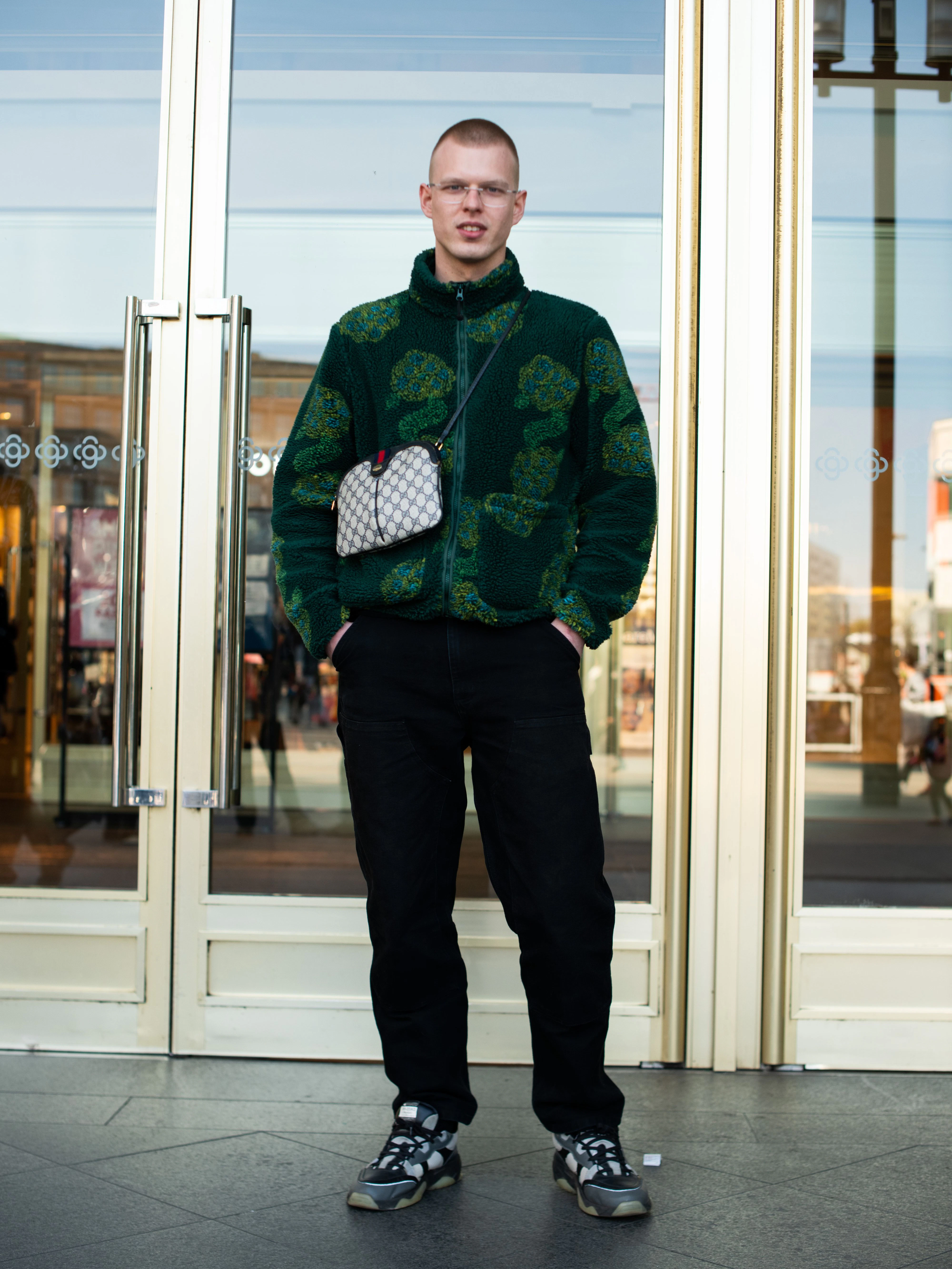 Noé ist gebürtiger Luxemburger. Derzeit lebt er in Berlin, um Verfahrenstechnik zu studieren. Hier am Alexanderplatz beeindruckt er mit herausragender Style-Kompetenz: Gemusterte Teddy-Jacke von Stüssy, Hose von Carhartt WIP, Sneakers des schwedischen Labels Axel Arigato und eine Gucci-Tasche.