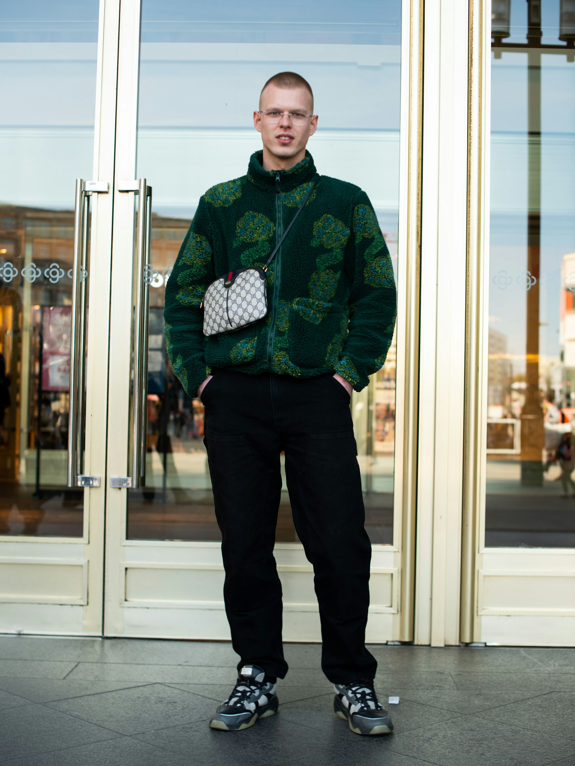 Noé ist gebürtiger Luxemburger. Derzeit lebt er in Berlin, um Verfahrenstechnik zu studieren. Hier am Alexanderplatz beeindruckt er mit herausragender Style-Kompetenz: Gemusterte Teddy-Jacke von Stüssy, Hose von Carhartt WIP, Sneakers des schwedischen Labels Axel Arigato und eine Gucci-Tasche.