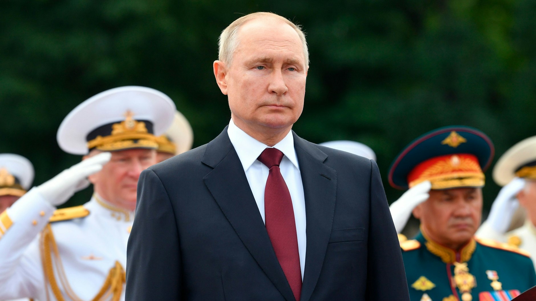 Wladimir Putin (M.), Präsident von Russland, hält seine Rede, während Admiral Nikolai Jewmenow (l.), Oberbefehlshaber der russischen Marine, und Sergej Schoigu (r.), Verteidigungsminister von Russland, bei einer Parade zum Tag der Marine salutieren. Ein Bild aus dem Jahr 2021.