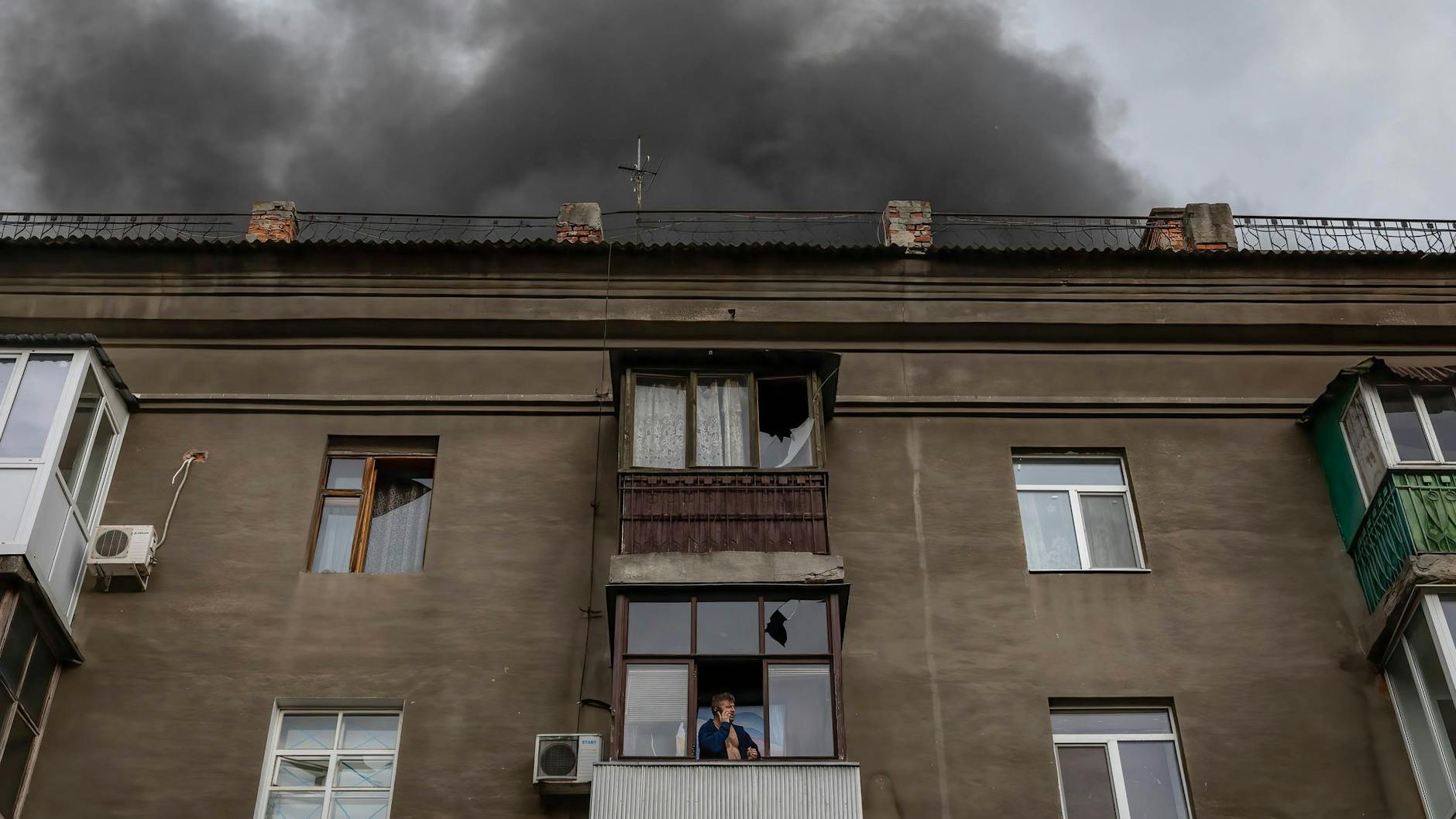 Ein Mann in der ukrainischen Stadt Charkiw telefoniert seelenruhig auf seinem Balkon, während das Dach des Hauses Feuer gefangen hat.
