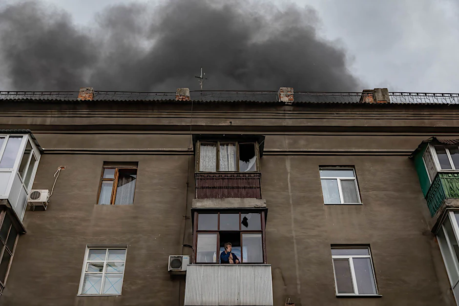 Ein Mann in der ukrainischen Stadt Charkiw telefoniert seelenruhig auf seinem Balkon, während das Dach des Hauses Feuer gefangen hat. 